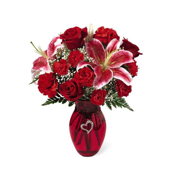 Charmez-la avec ce bouquet romantique de roses et d'oeillets rouges,  d'oeillets miniatures et de magnifiques lys du Japon. Le vase de verre  soufflé est décoré d'un simple coeur métallique scintillant.